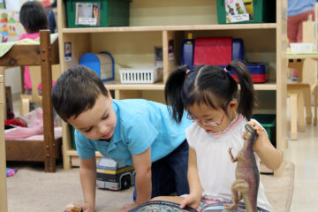 Little brown-haired white boy and Asian girl with Down syndrome reading books.