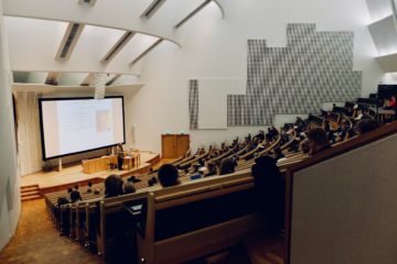 Large classroom with lots of seats and a professor up front.