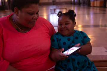 Black girl with Down syndrome showing her mother an iPad.
